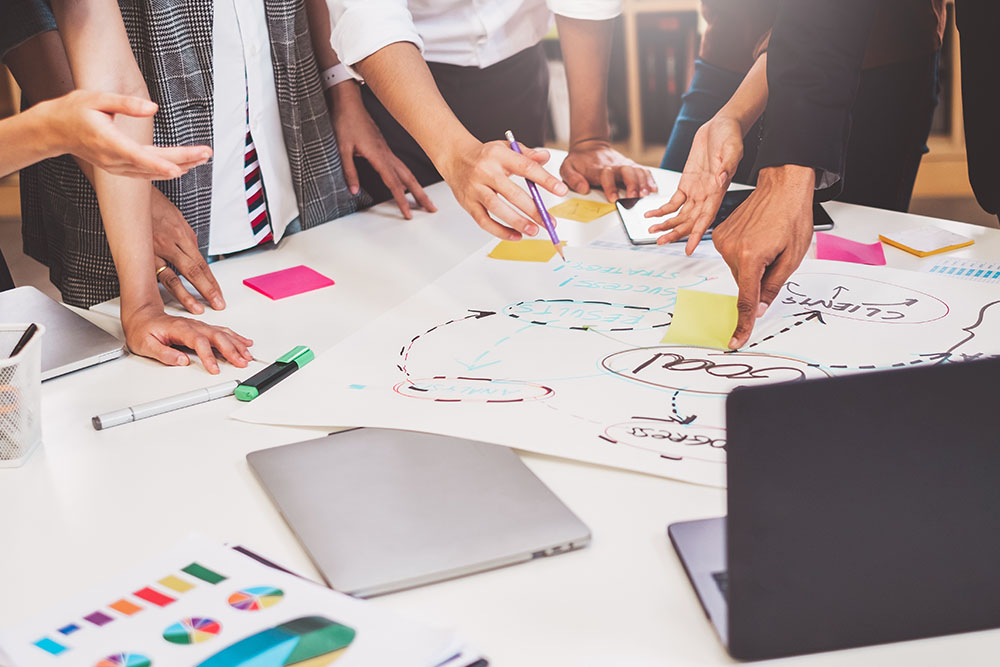 Tisch mit mehreren Personen, von denen nur die Hände zu sehen sind, die eine Mindmap besprechen.